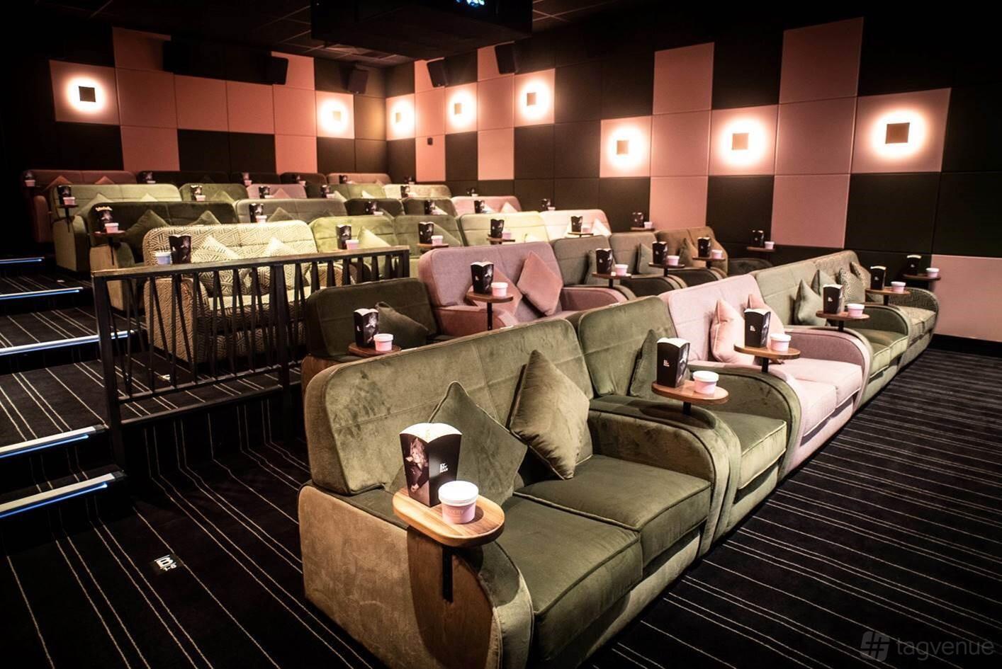 An auditorium with plush green sofas, small wooden tables, and wall sconces at Everyman Cardiff.