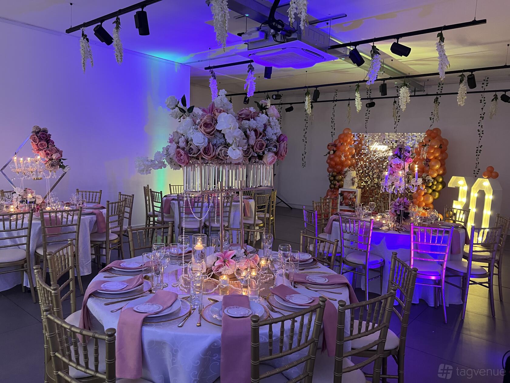 A gallery function room with round tables, gold chairs, pink floral centerpieces, and decorative lighting at The Old Street Gallery.