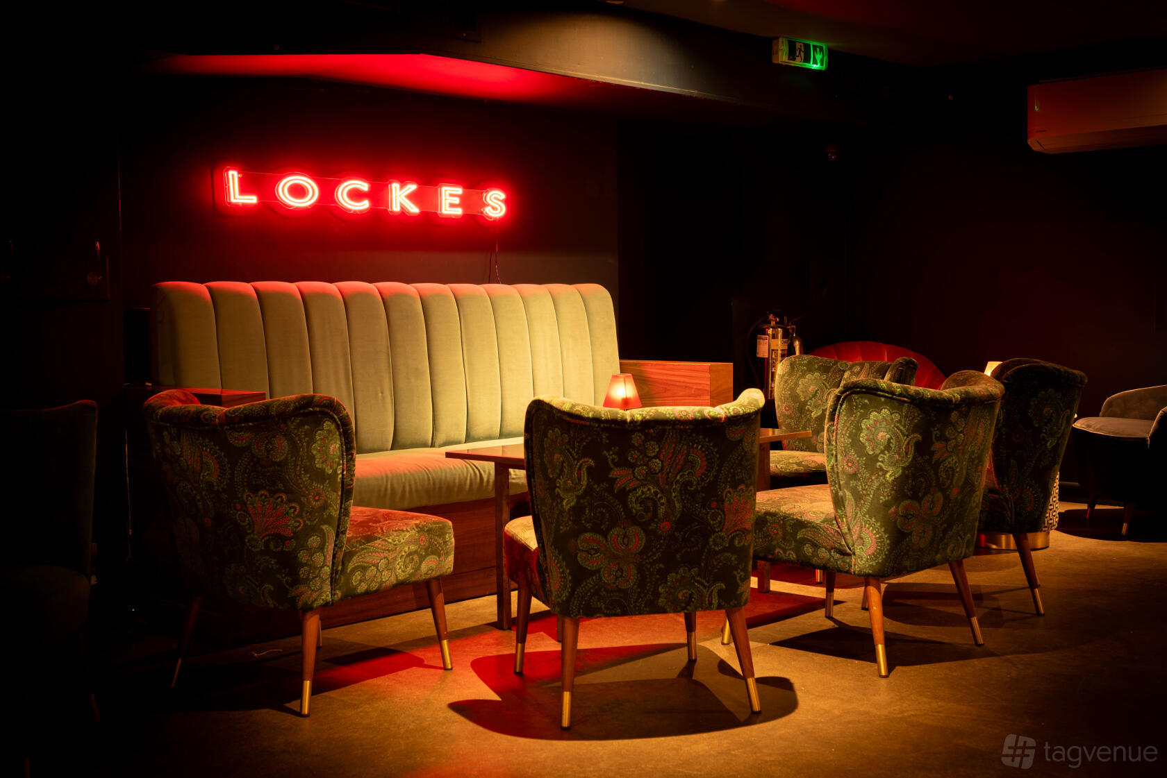An underground cocktail bar with velvet armchairs, a tufted banquette, and red neon lighting at LOCKES Bar Covent Garden.