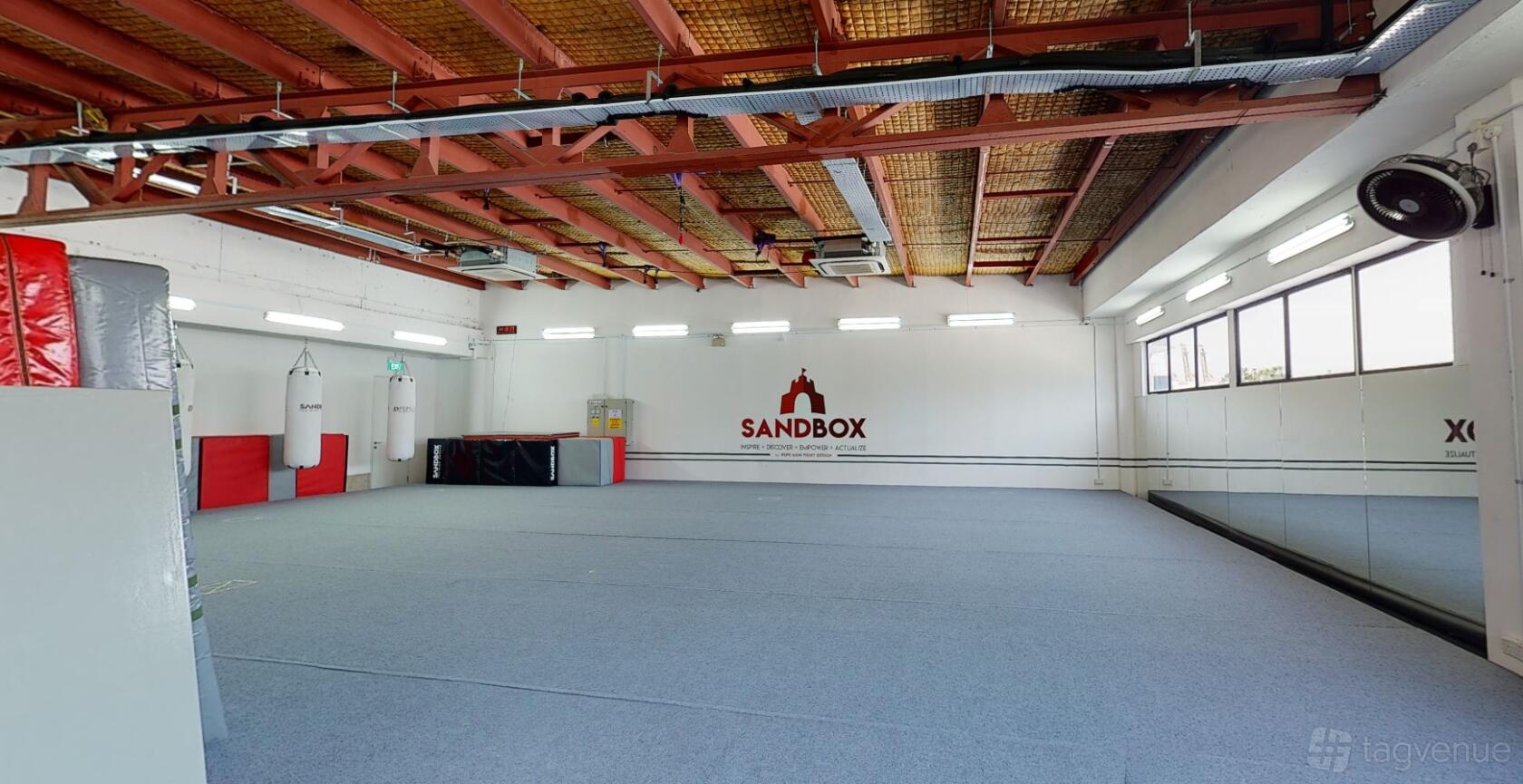 An event space with padded flooring, exposed ceiling beams, and wall mirrors at Sandbox Training Ground.