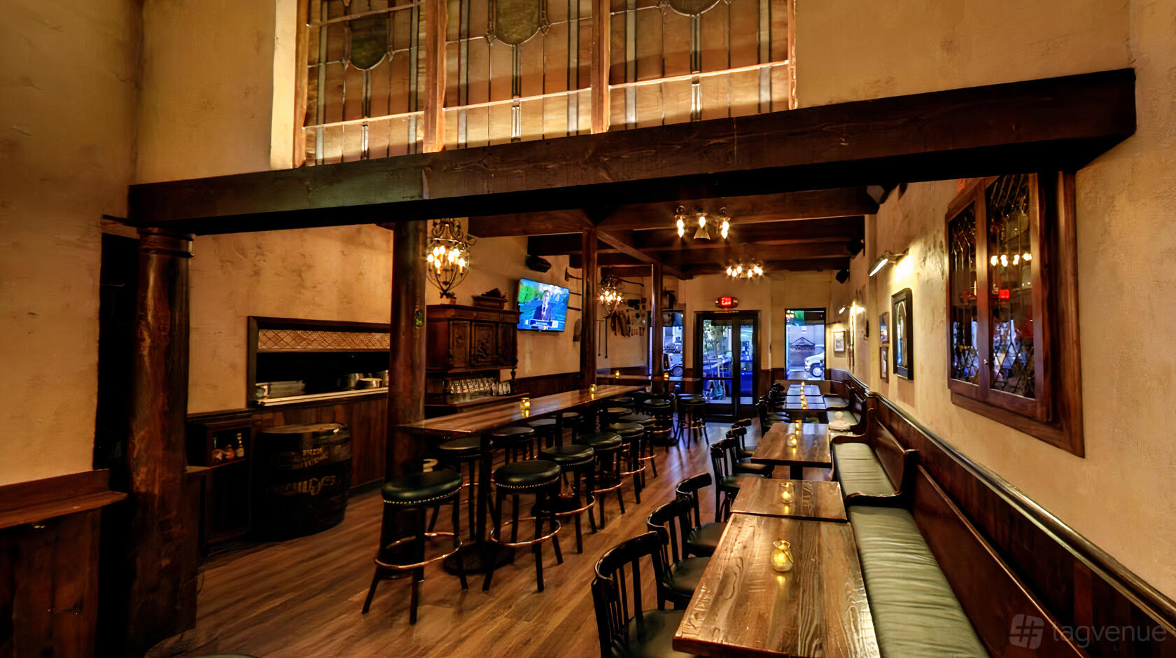 An event space in a pub with long wooden tables, barstools, chandeliers, and a large stained glass panel at Chief Sullivan's.