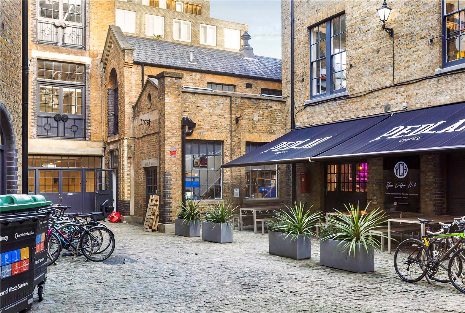 A film and photo studio with a cobblestone courtyard, brick buildings, outdoor seating, and potted plants at UP Studios.