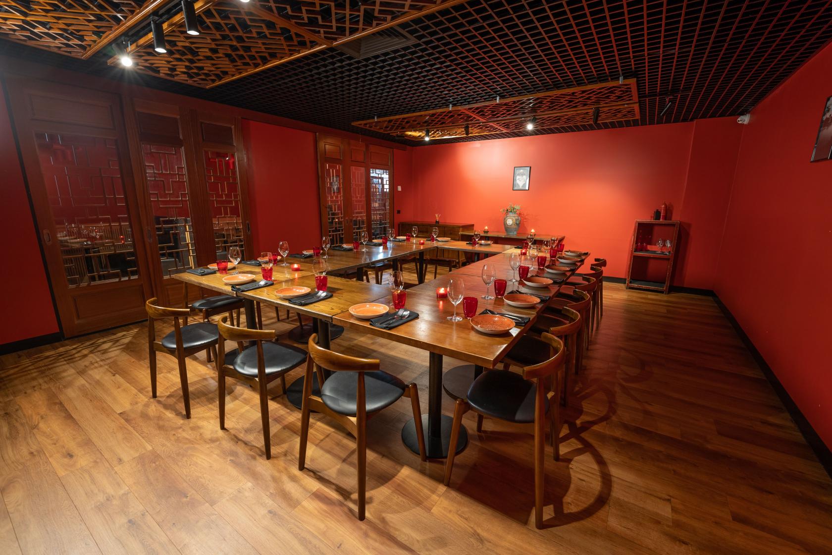 A dining room with red walls, wooden floors, a large U-shaped table set with red glassware at Red Spice Road.