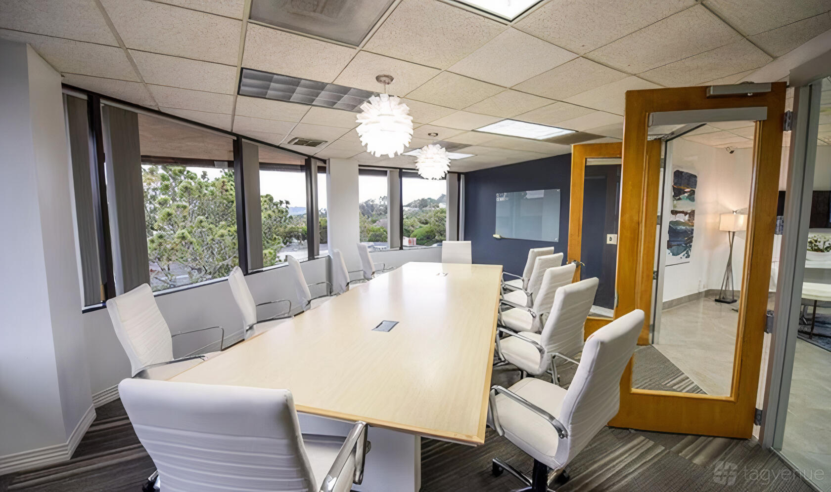 A boardroom with a long light wood table, white swivel chairs, and large windows at Premier Workspaces - Plaza Del Mar.