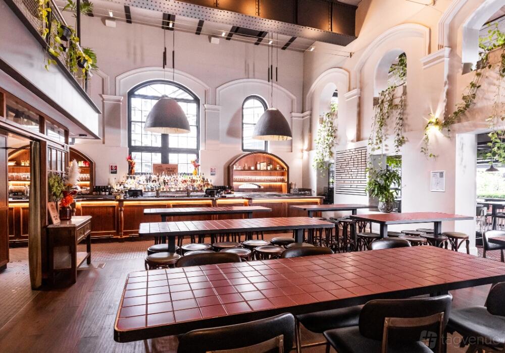 An event space in a pub with high arched windows, hanging pendant lights, and tiled tables at Pumphouse Sydney.