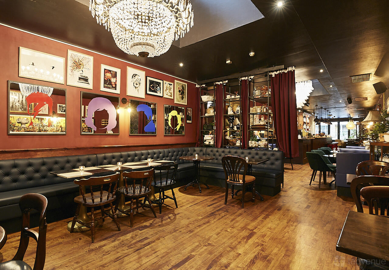 A lounge with tufted banquette seating, wooden tables, a chandelier, and wall art at Little Bat Bar & Kitchen.