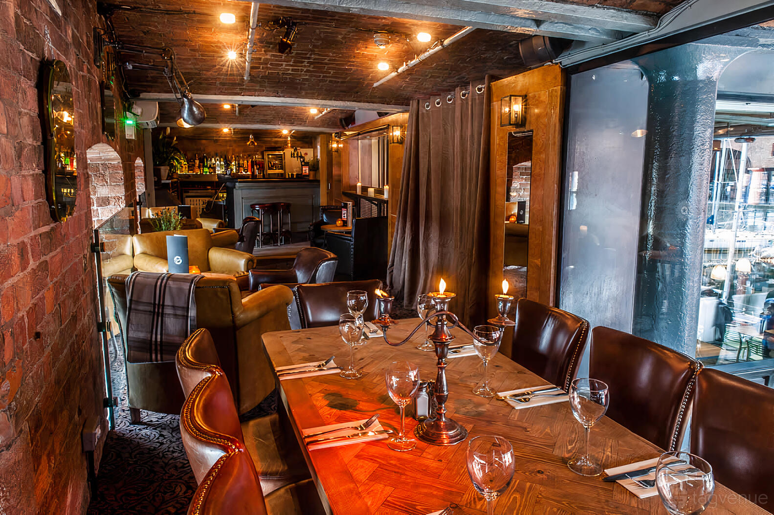 A mezzanine bar with exposed brick walls, leather chairs, and a wooden dining table at Revolution Liverpool Albert Dock.