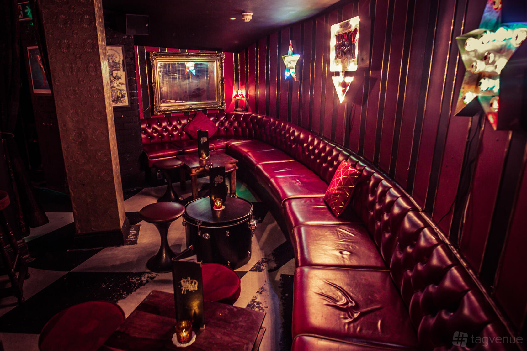 A cocktail bar with red leather banquette seating, dark wood walls, and eclectic wall lighting at The Cocktail Club Liverpool Street.