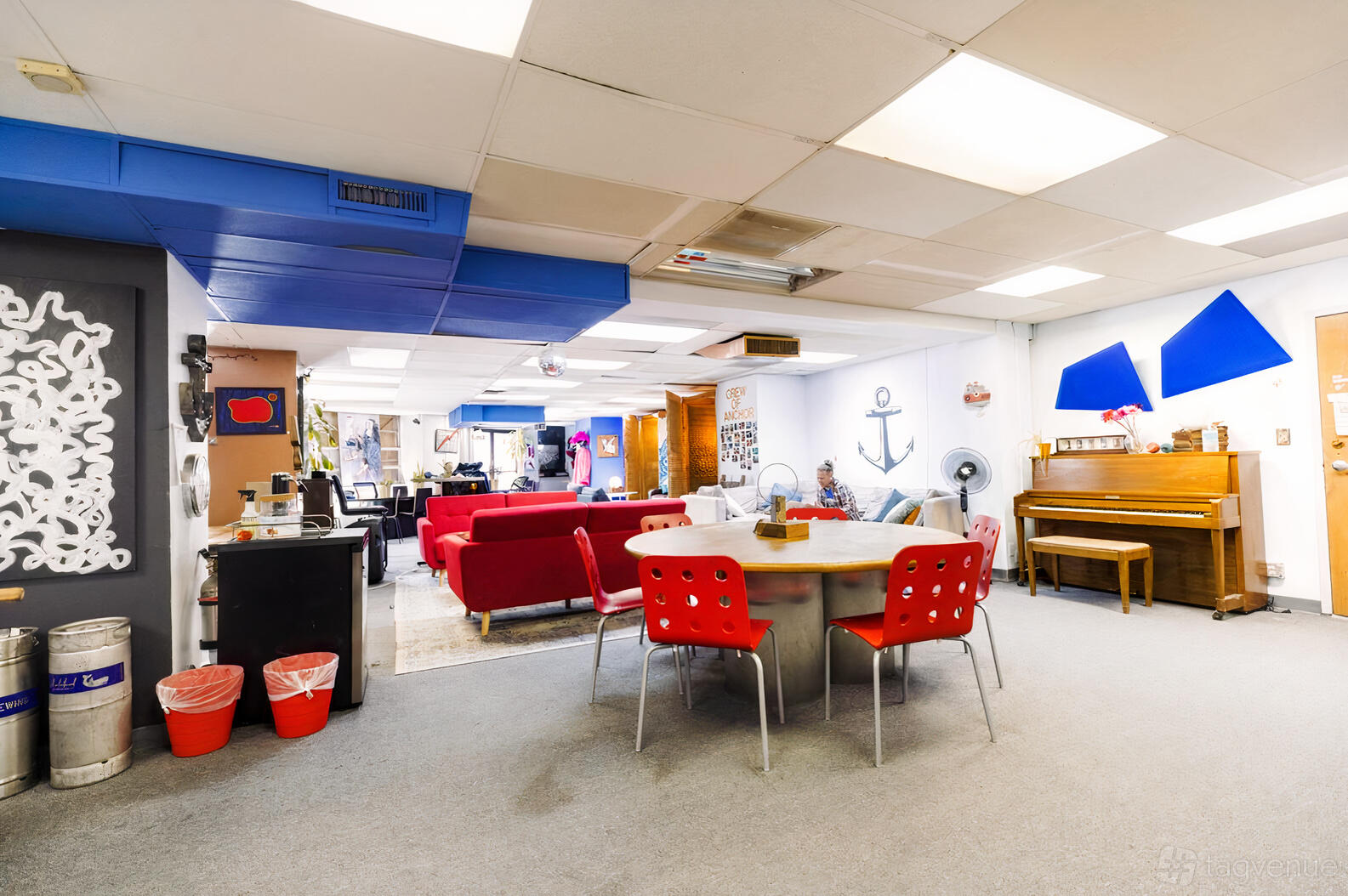 An event space with red chairs, round tables, a lounge area with sofas, and a piano at Anchor.