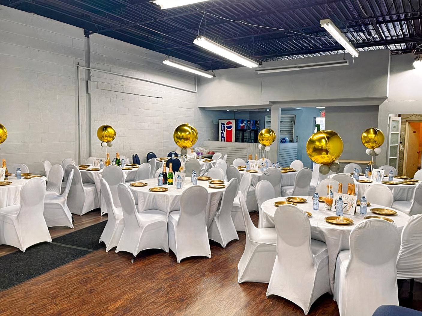 An event venue with round tables draped in white linens, gold balloons, and banquet chairs at Finch Party House.