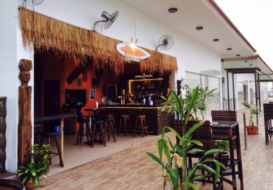 A thatched-roof bar with wooden stools, rattan tables, and potted plants at Georges By The Bay (Punggol).