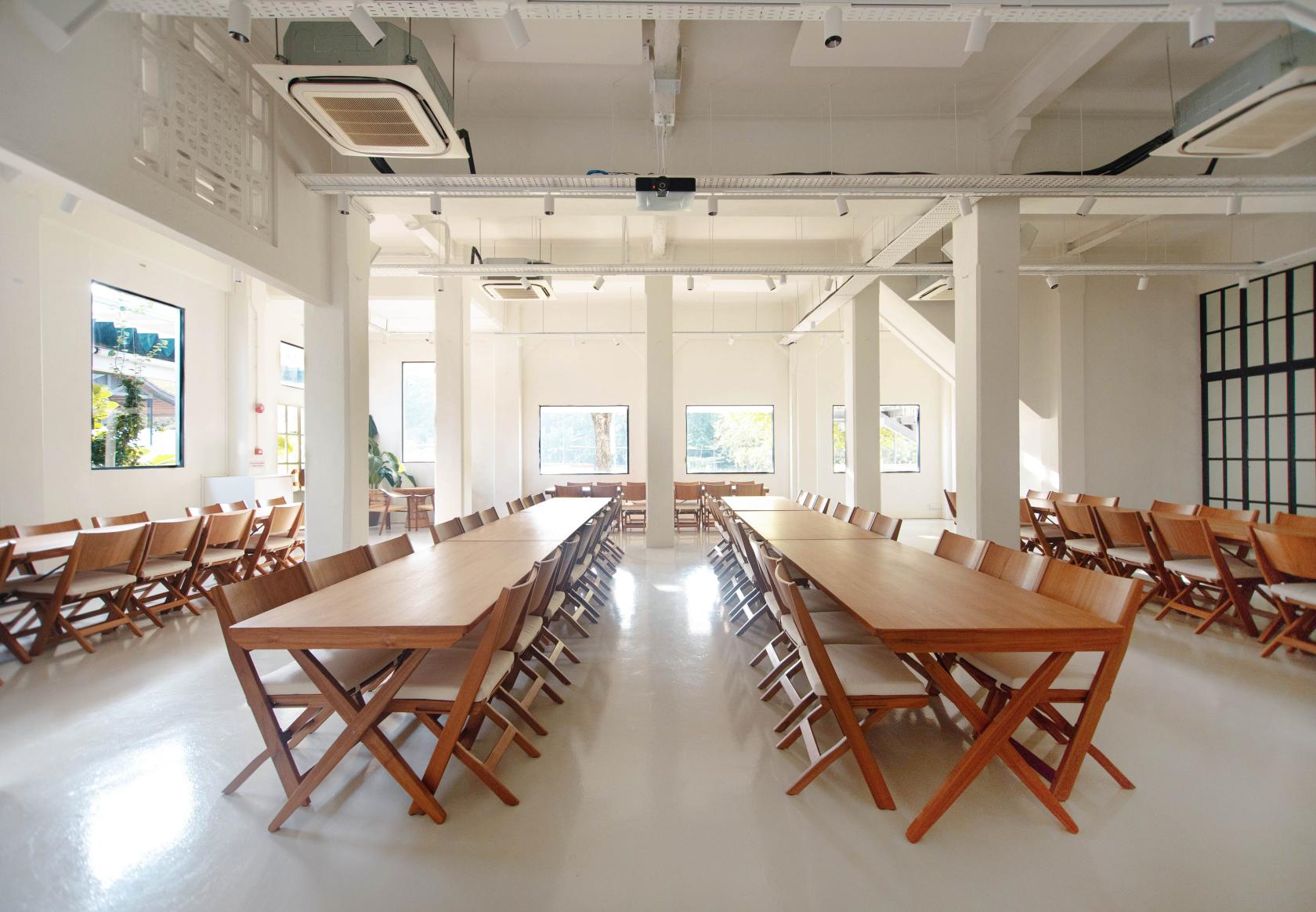 An event venue with long wooden tables, folding chairs, large windows, and polished floors at Ida's Event Space.
