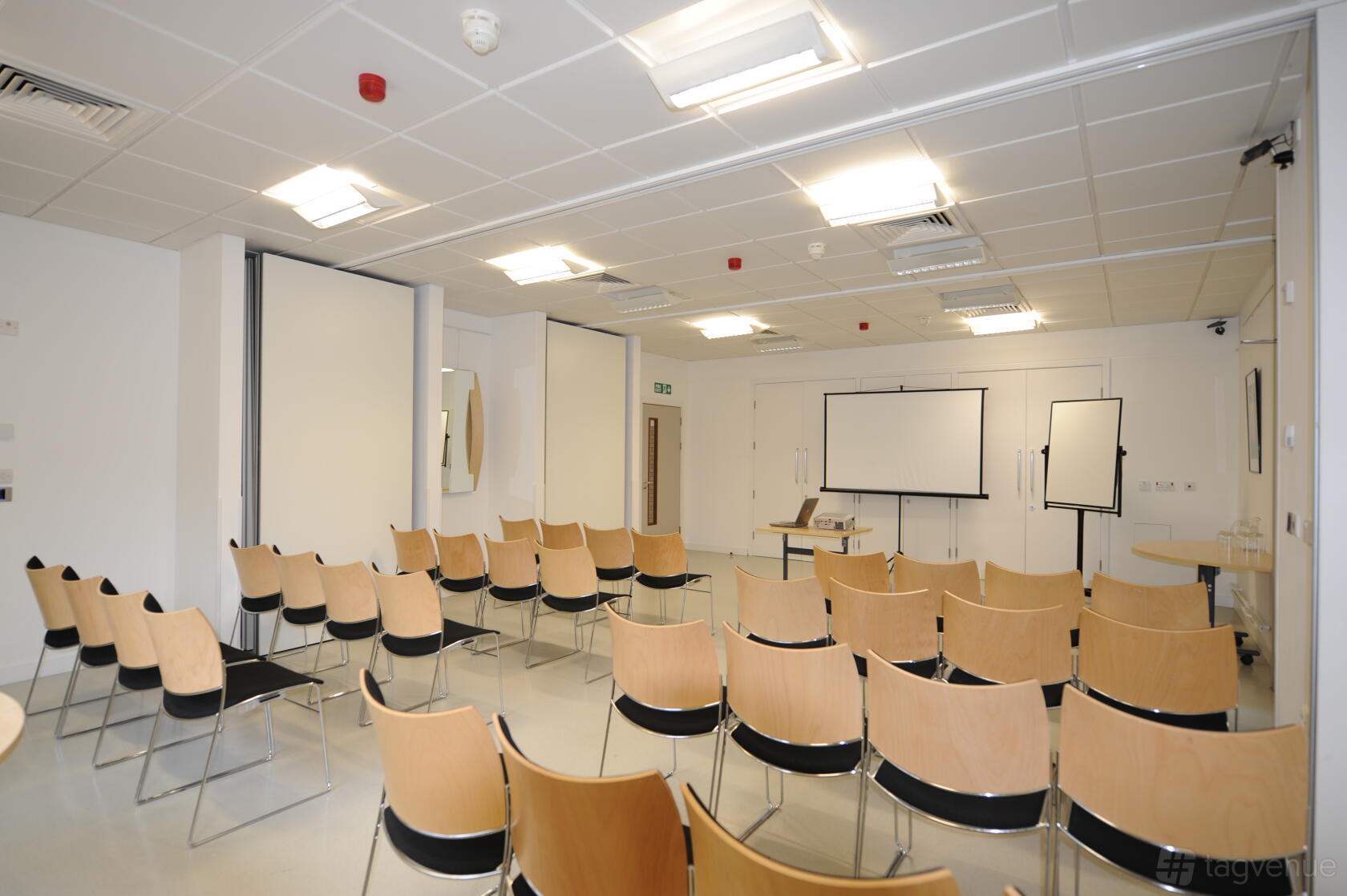 A conference centre room with rows of light wood chairs, white walls, and presentation screens at Signing Tree Venue.
