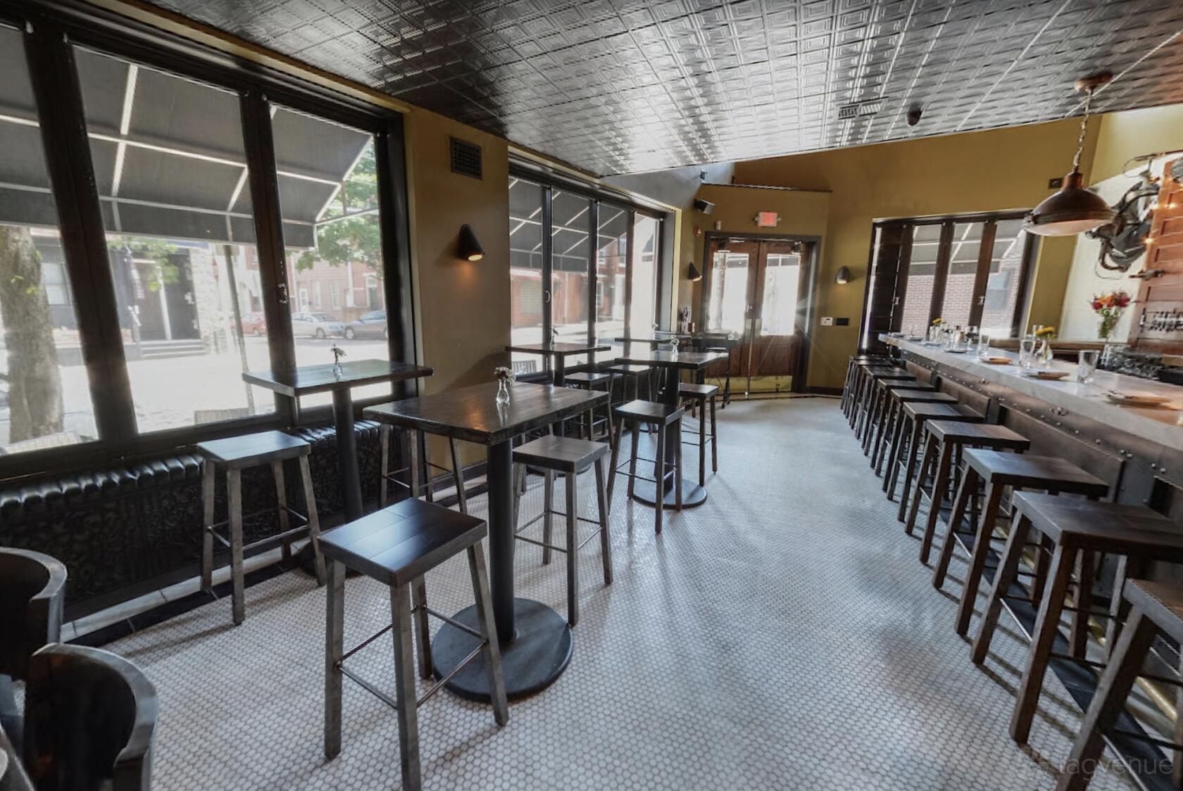 A bar with high-top tables, black stools, a long bar counter, and large front windows at Jerry's Bar.