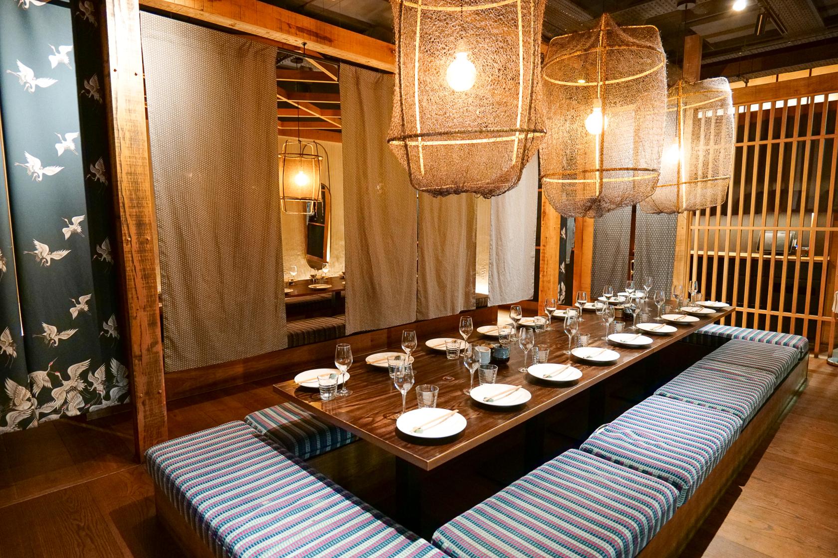 A private dining room with a long wooden table, striped bench seating, and hanging woven light fixtures at Flesh and Buns Oxford Circus.
