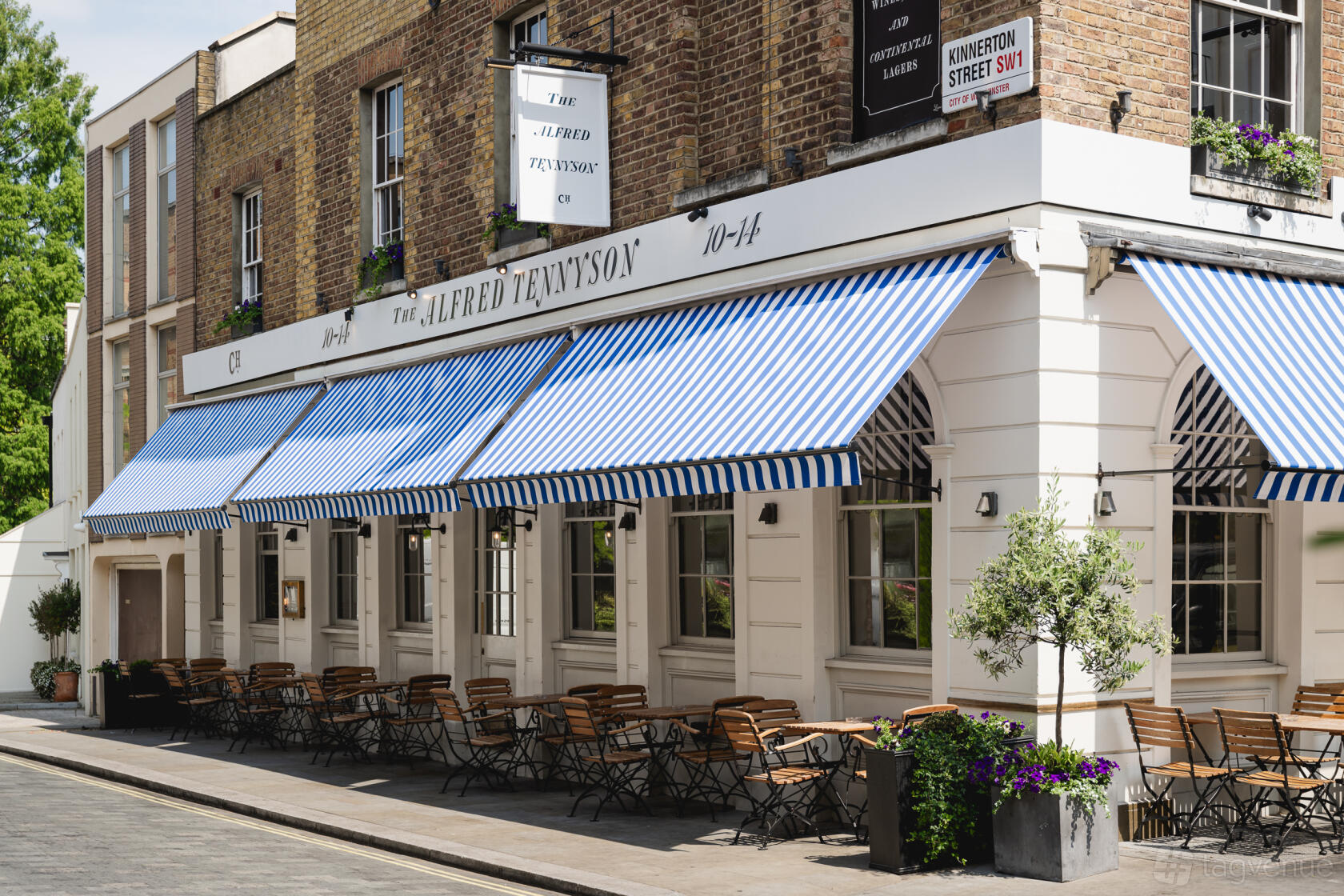 A pub with striped blue awnings, brick exterior walls, and outdoor seating at The Alfred Tennyson Belgravia.