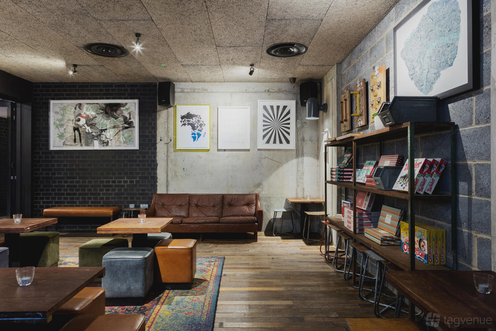 A function room in a bar with a leather sofa, artwork, wooden tables, and game shelves at Heist Bank.