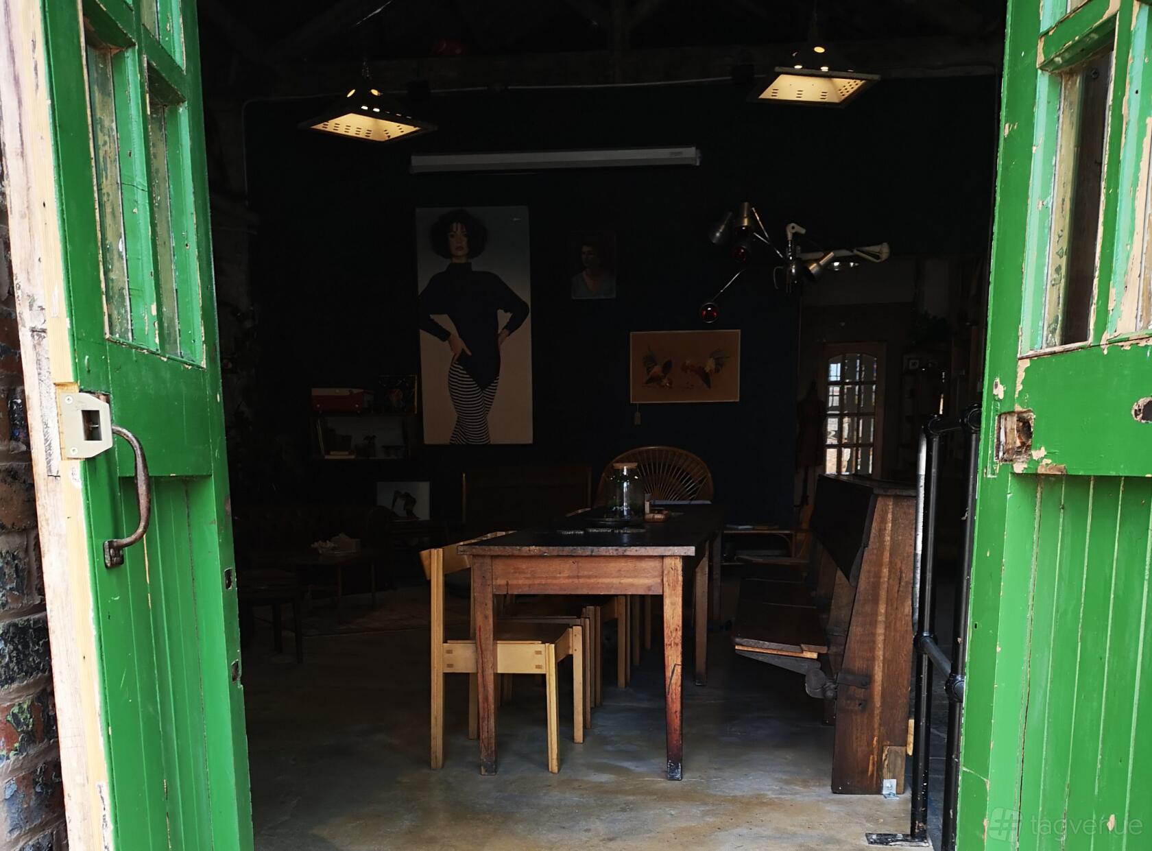 A cafe with wooden tables, benches, eclectic art on dark walls, and green double doors at Artefact.