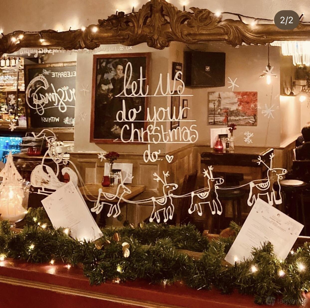 A pub decorated with festive garlands, hand-drawn reindeer, and holiday lettering on glass at The Prince of Wales Feathers.