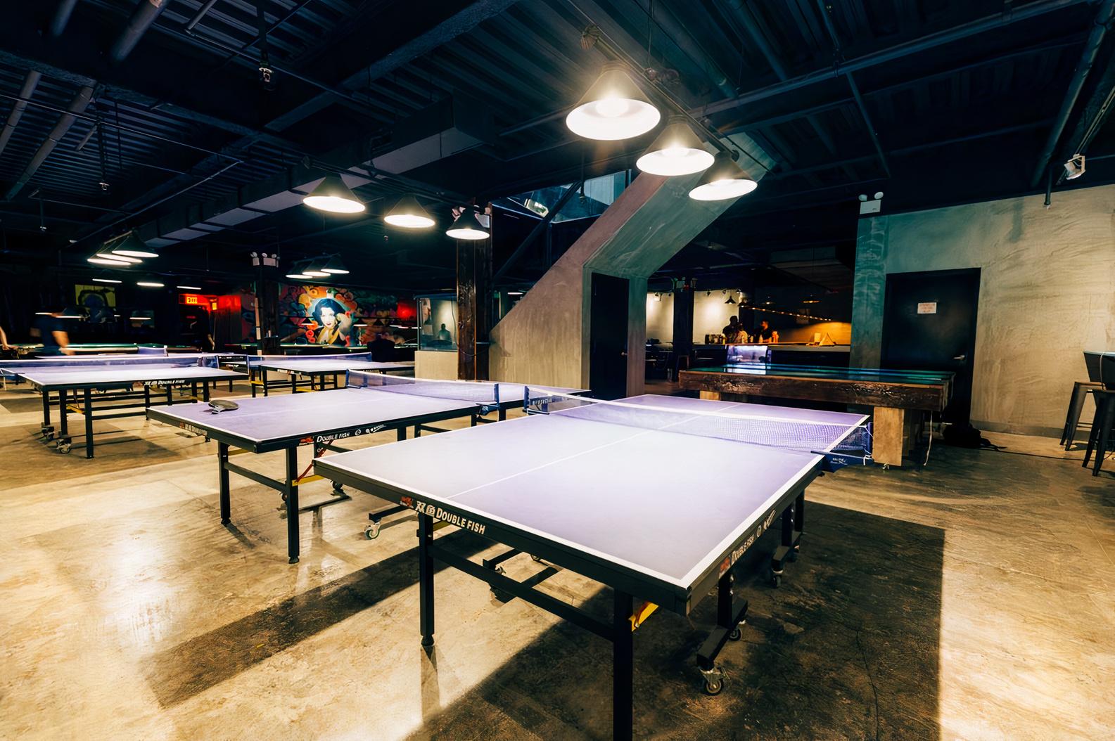 An event space in a bar with multiple ping pong tables, concrete floors, and industrial pendant lighting at Sour Mouse.