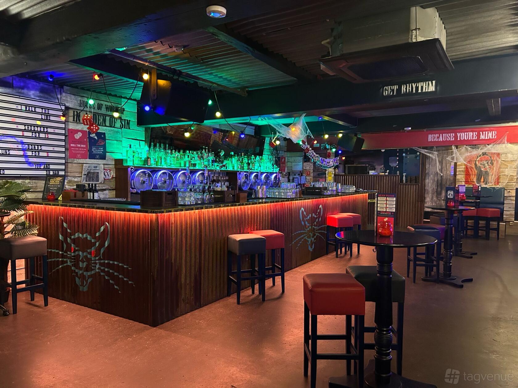 A bar with neon lighting, high tables, industrial ceiling, and a corrugated counter at Mean Eyed Cat Liverpool.