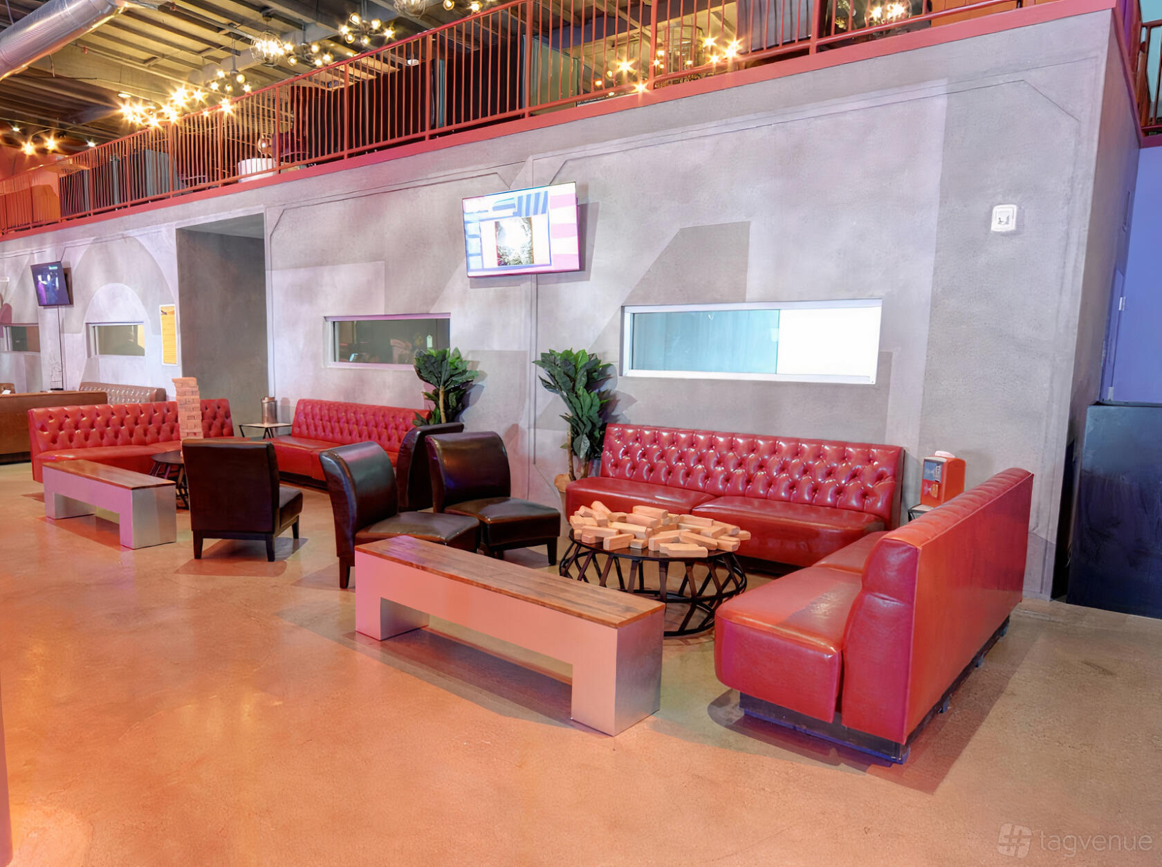 An event venue lounge with red tufted sofas, leather chairs, plants, and a Jenga game table at Two Bit Circus.