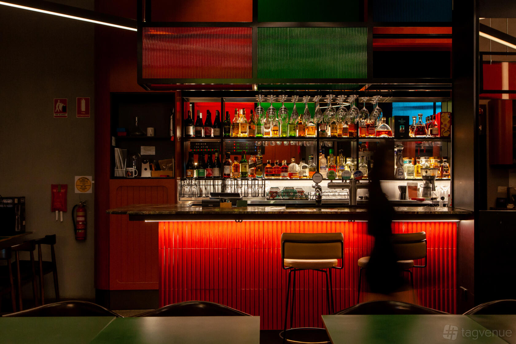A restaurant with a backlit bar, colorful shelving, and high stools at Yum Sing House.
