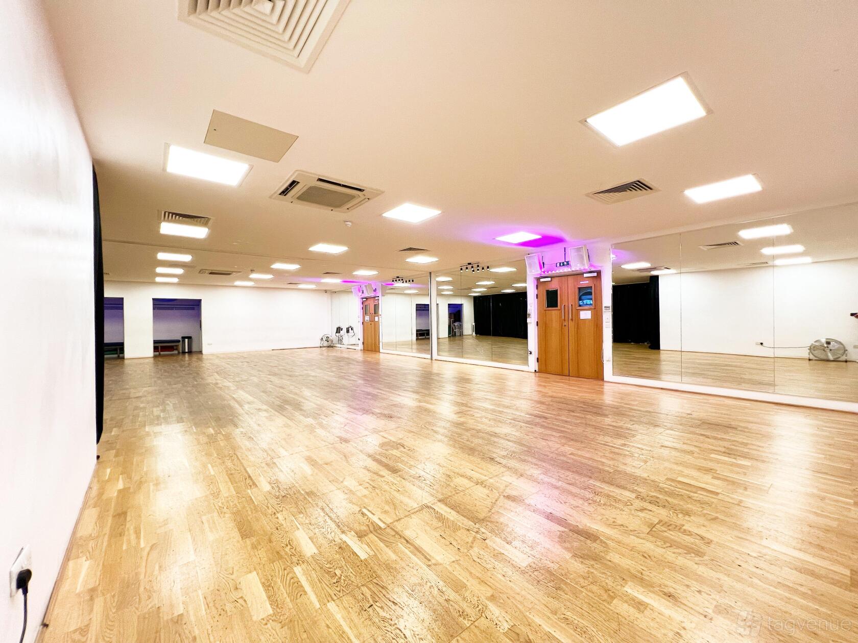 A dance studio with mirrored walls, wooden floors, and bright ceiling lights at UNIT 3.