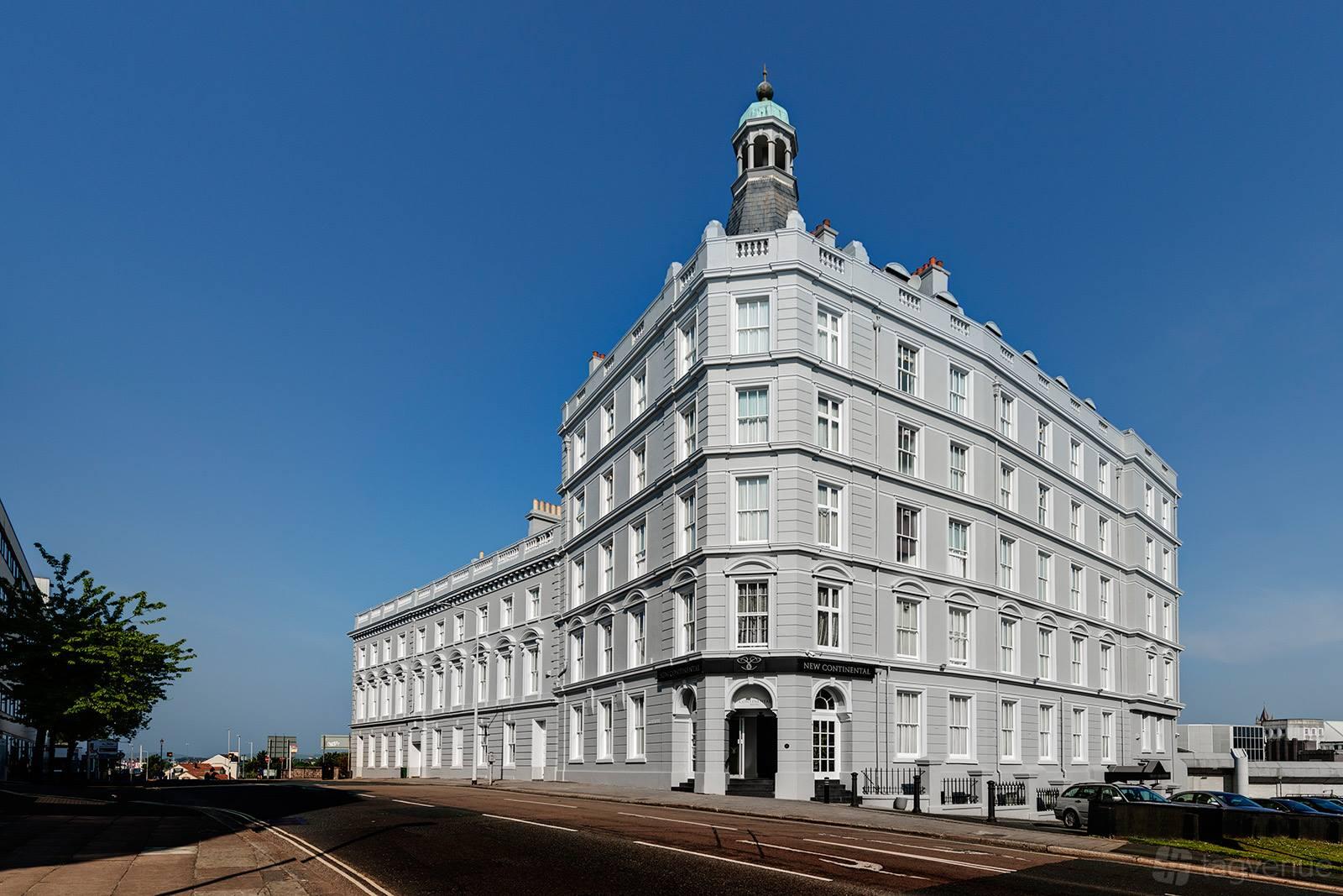 A historic hotel with a white facade, arched windows, and corner tower at New Continental Hotel.