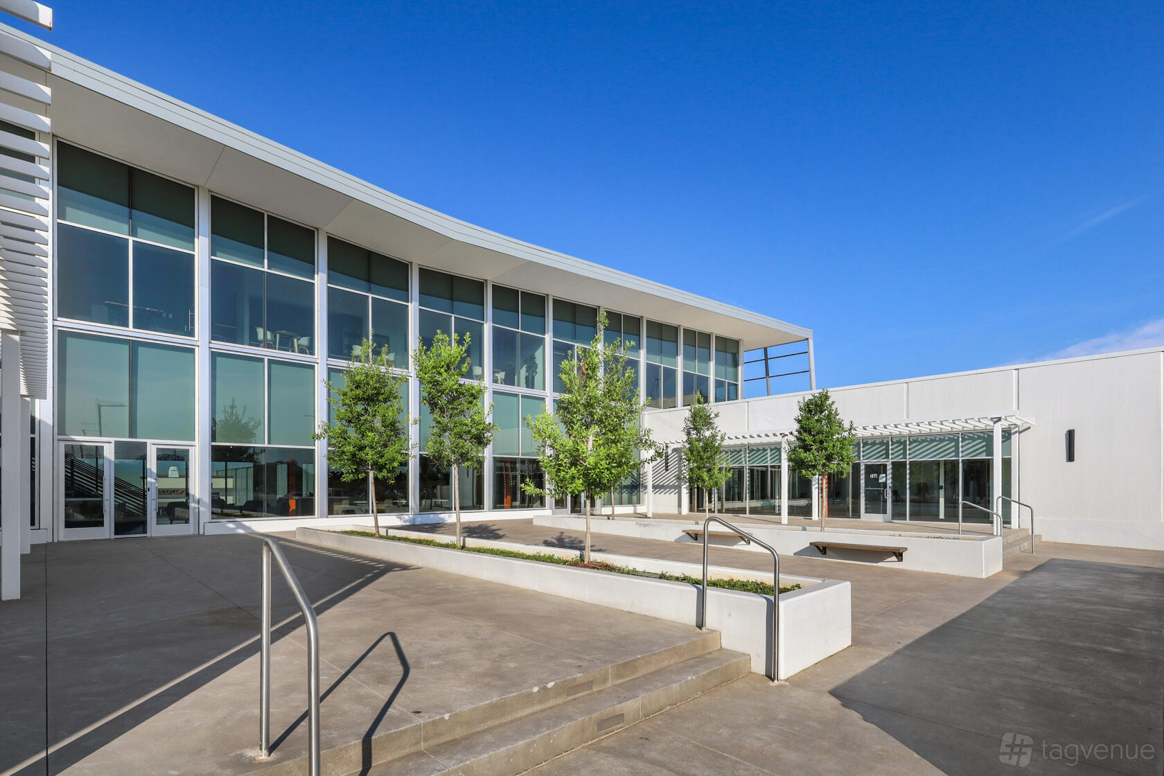 A versatile event space with large floor-to-ceiling windows, concrete courtyard, and landscaped trees at Venture X Dallas – Braniff Centre.