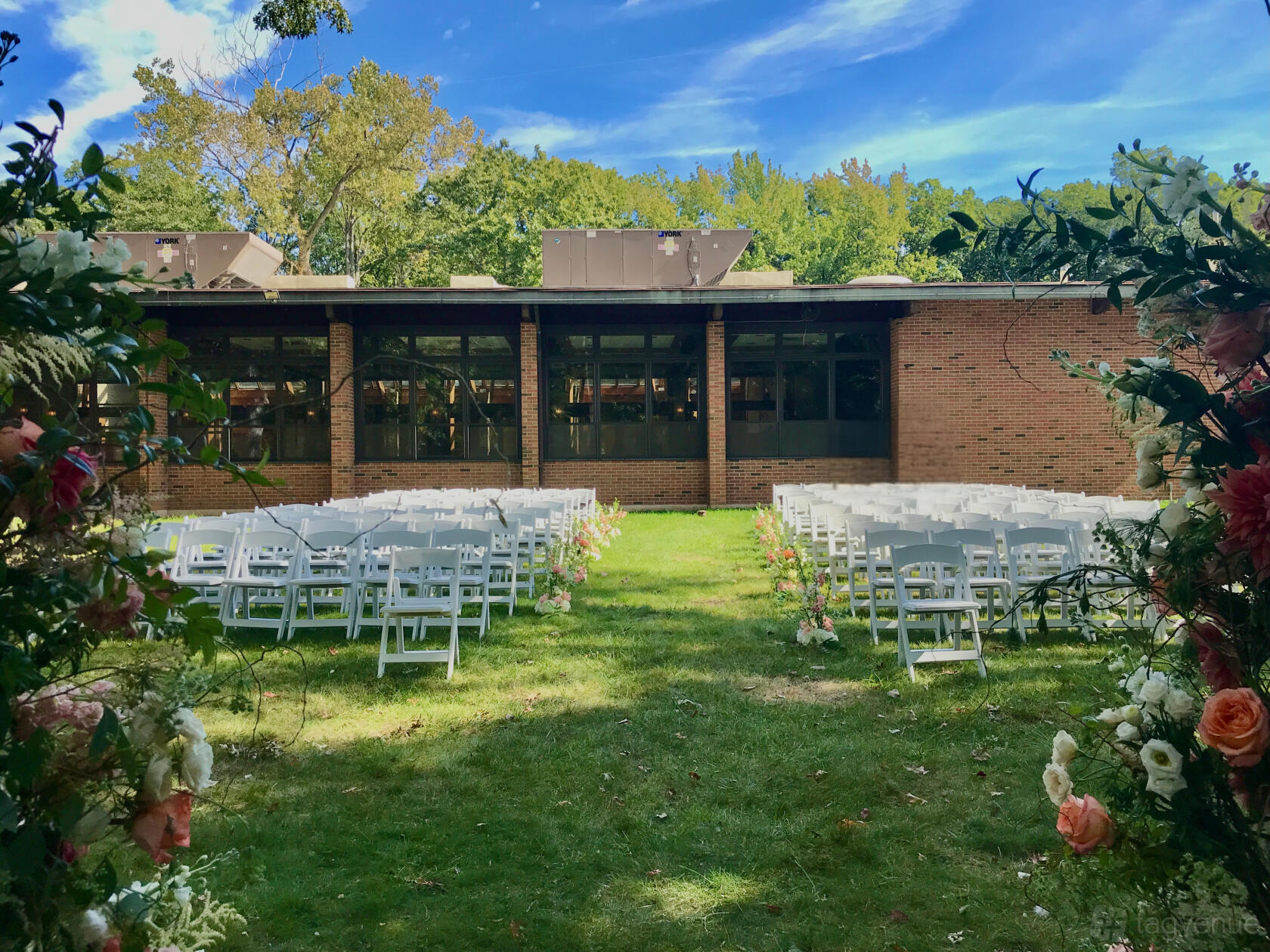 A grassy outdoor ceremony area with rows of white folding chairs and floral arrangements at Atrium of Tenafly.
