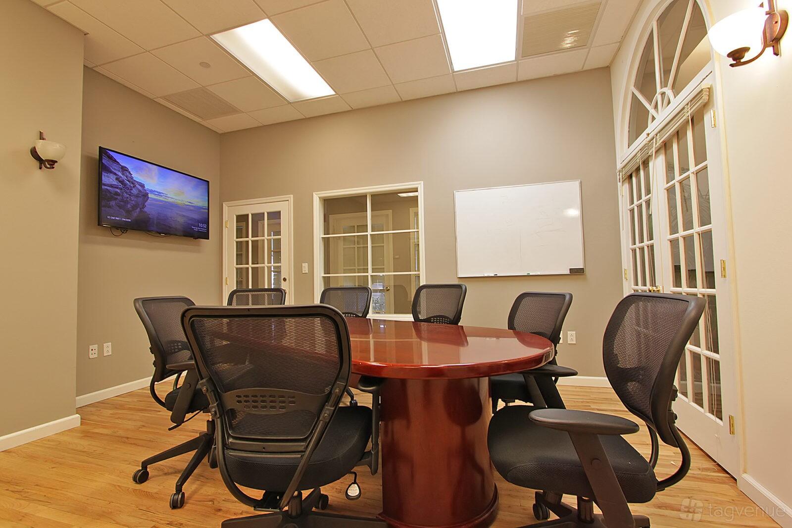 A meeting centre with a polished oval conference table, mesh office chairs, whiteboard, and wall-mounted screen at Select Office Suites Flatiron.