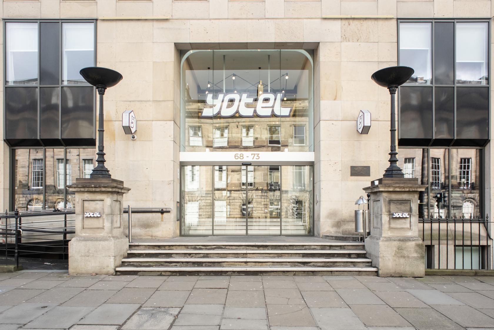 A hotel entrance with glass doors, modern signage, and stone pillars at YOTEL Edinburgh.
