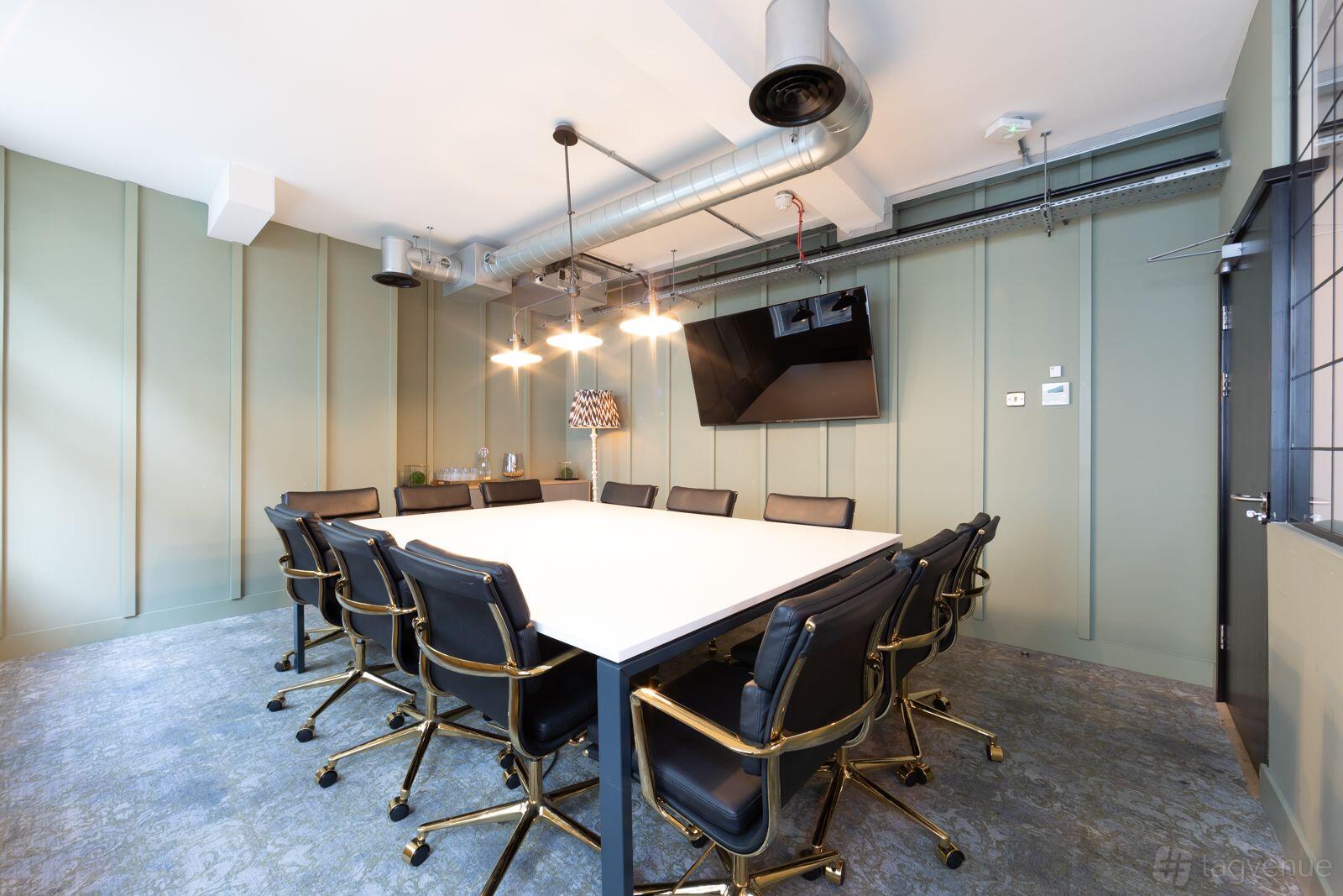 A meeting room with a large square table, black leather chairs, overhead pendant lighting, and a wall-mounted screen at The Space Regent Street.