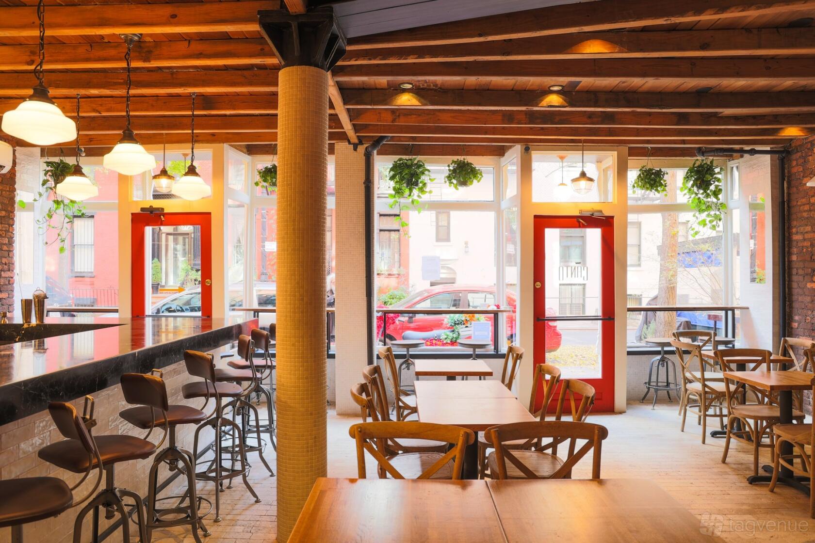 A restaurant with exposed wooden beams, hanging plants, large windows, and wooden tables at Canto.