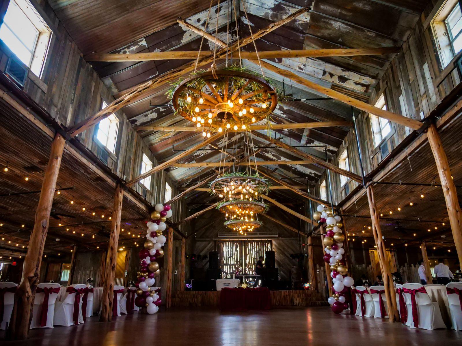 A rustic barn with exposed wooden beams, wagon wheel chandeliers, and balloon decorations at Rancho La Mission.