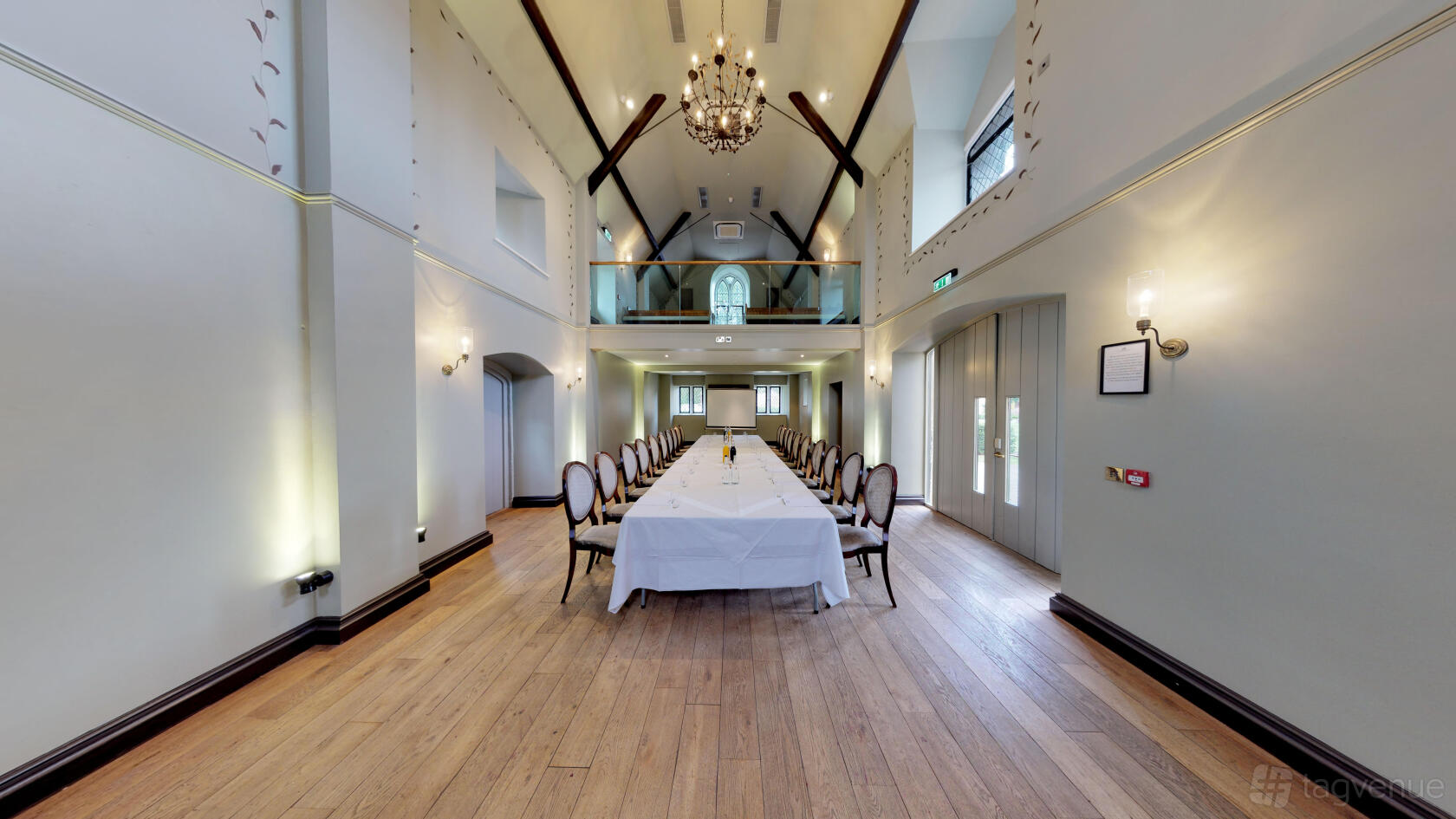 An event space with high vaulted ceilings, a long banquet table, chandeliers, and wood flooring at Ellenborough Park's The Chapel.