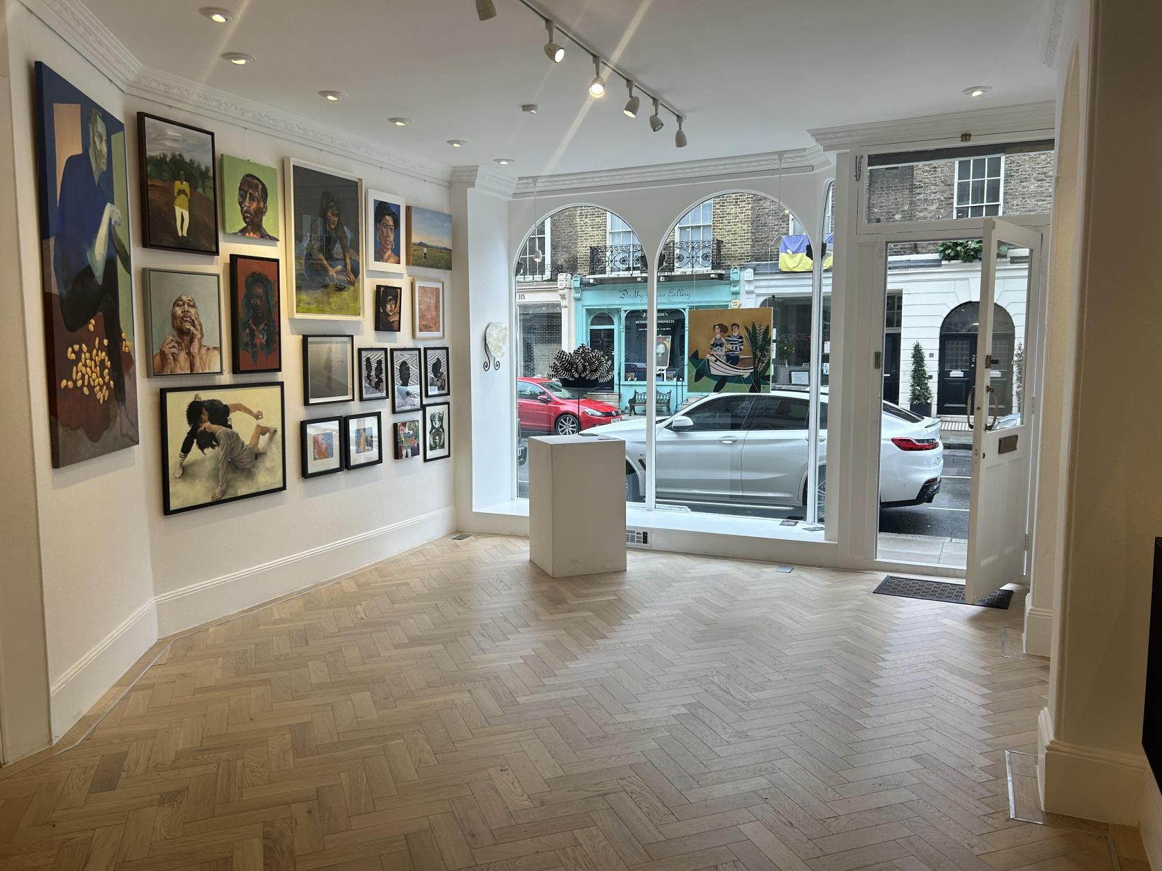 An art gallery with parquet floors, large front windows, and walls displaying colorful paintings at Casild Art.