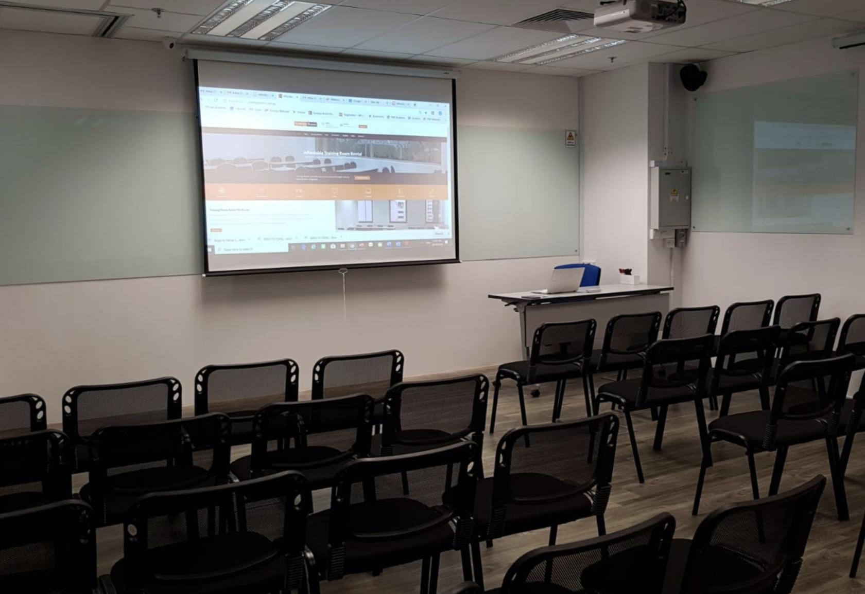 A training room with rows of black mesh chairs facing a projection screen and whiteboards at Synergy Room Havelock 2.