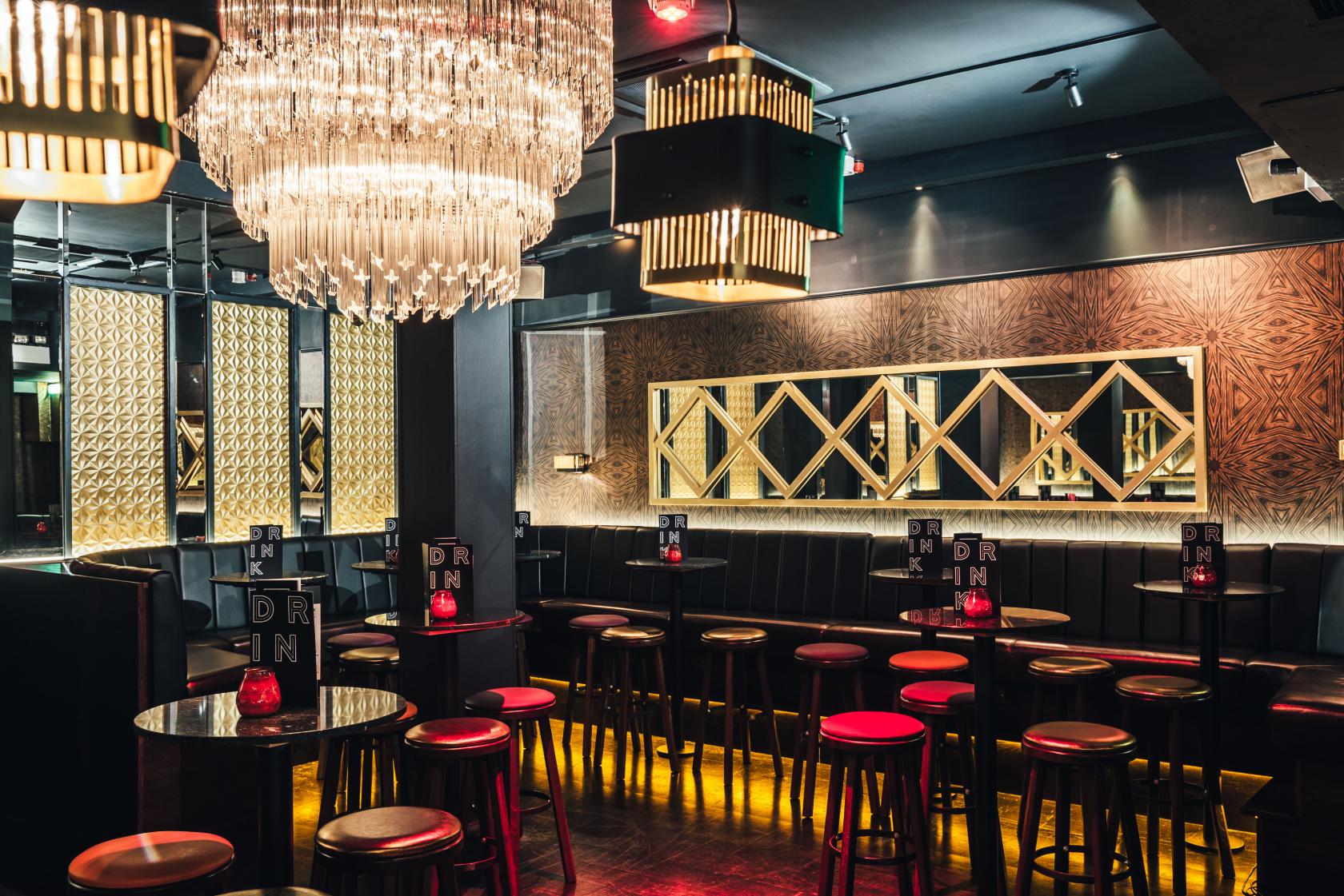 An event space in a bar with a chandelier, gold geometric wall panels, and black stools at Sway.