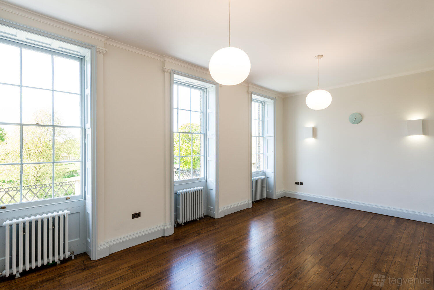 A country house room with large sash windows, globe pendant lights, and wooden floors at Clissold House.