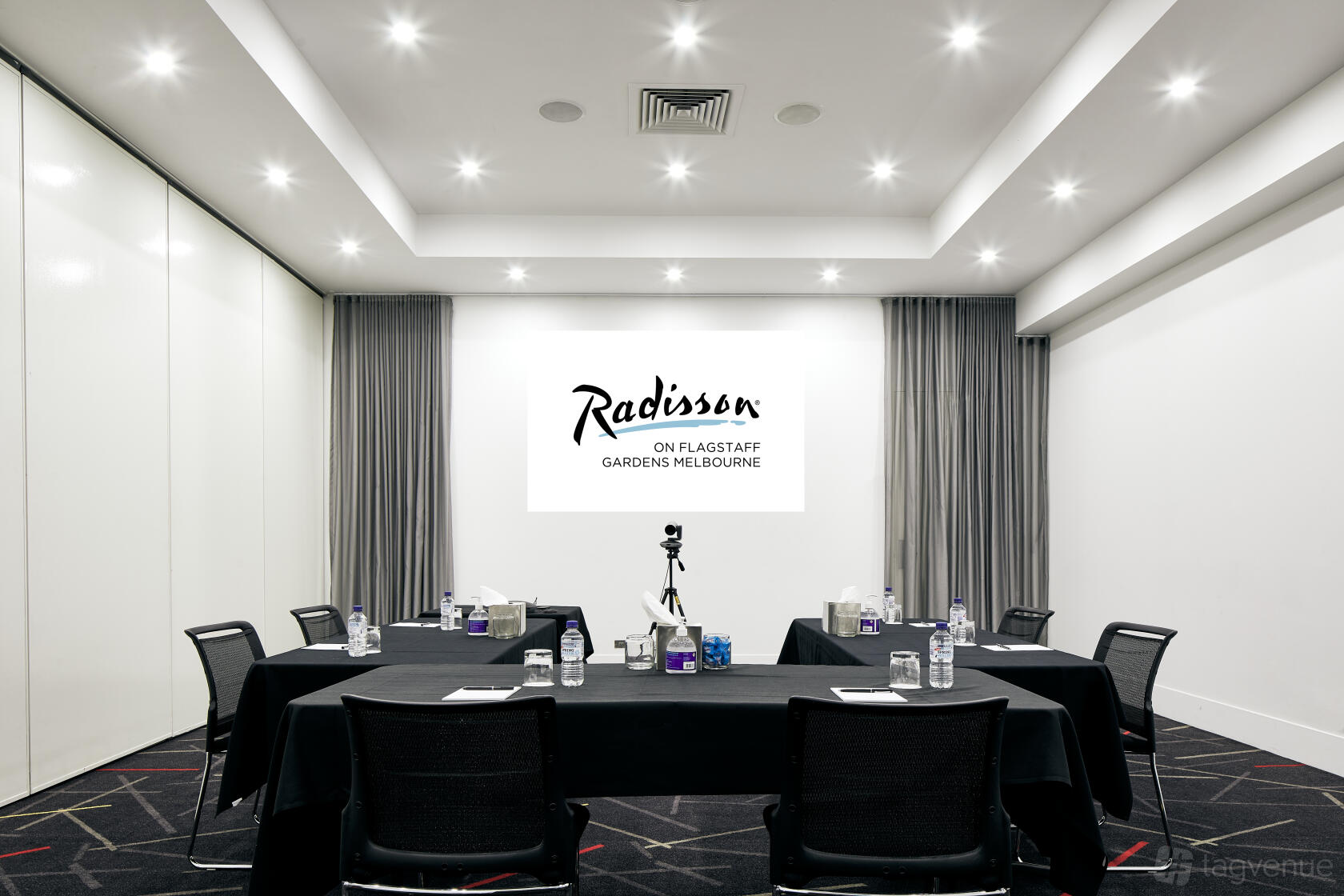 A meeting room with black tables, mesh chairs, and a ceiling-mounted projector at Radisson on Flagstaff Gardens Melbourne.