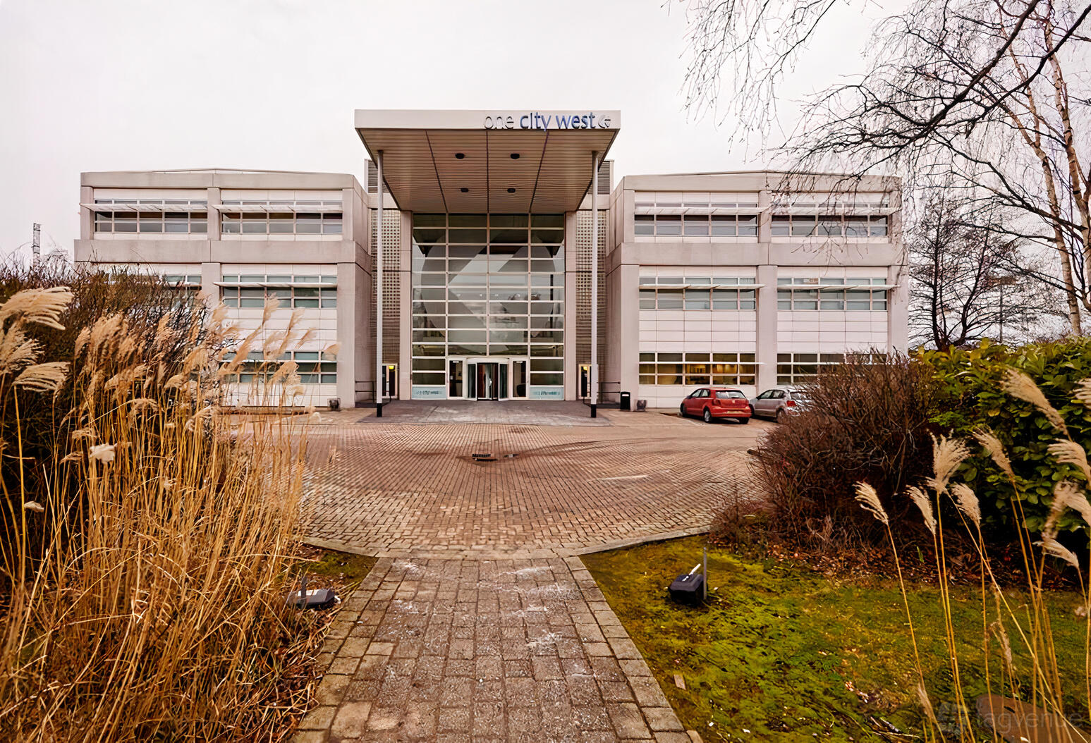 A conference centre with a glass-front entrance, wide paved driveway, and landscaped gardens at Biz Hub One City West.