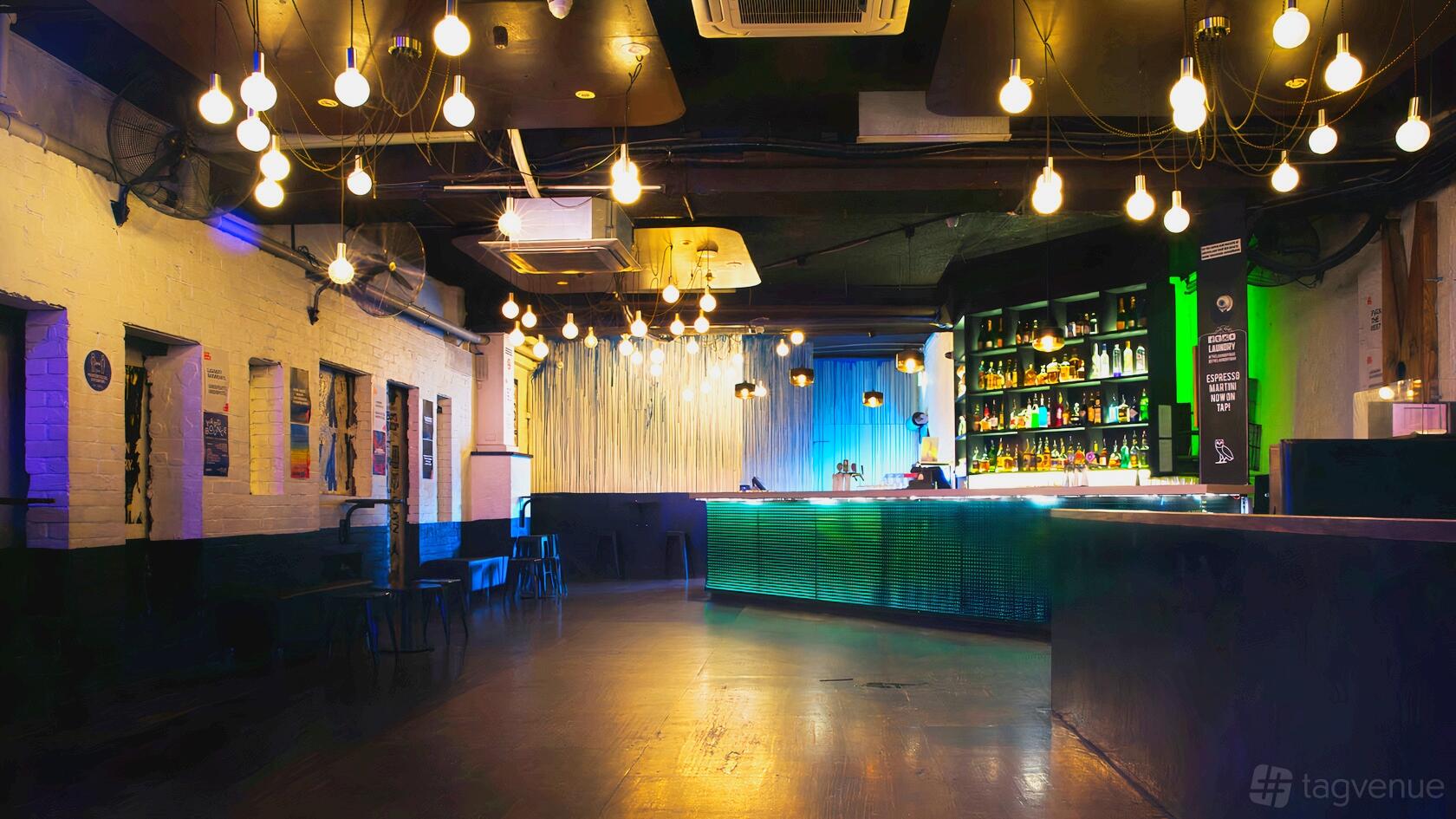 A nightclub bar with colorful backlit shelves, hanging pendant lights, and exposed brick walls at Laundry Bar.