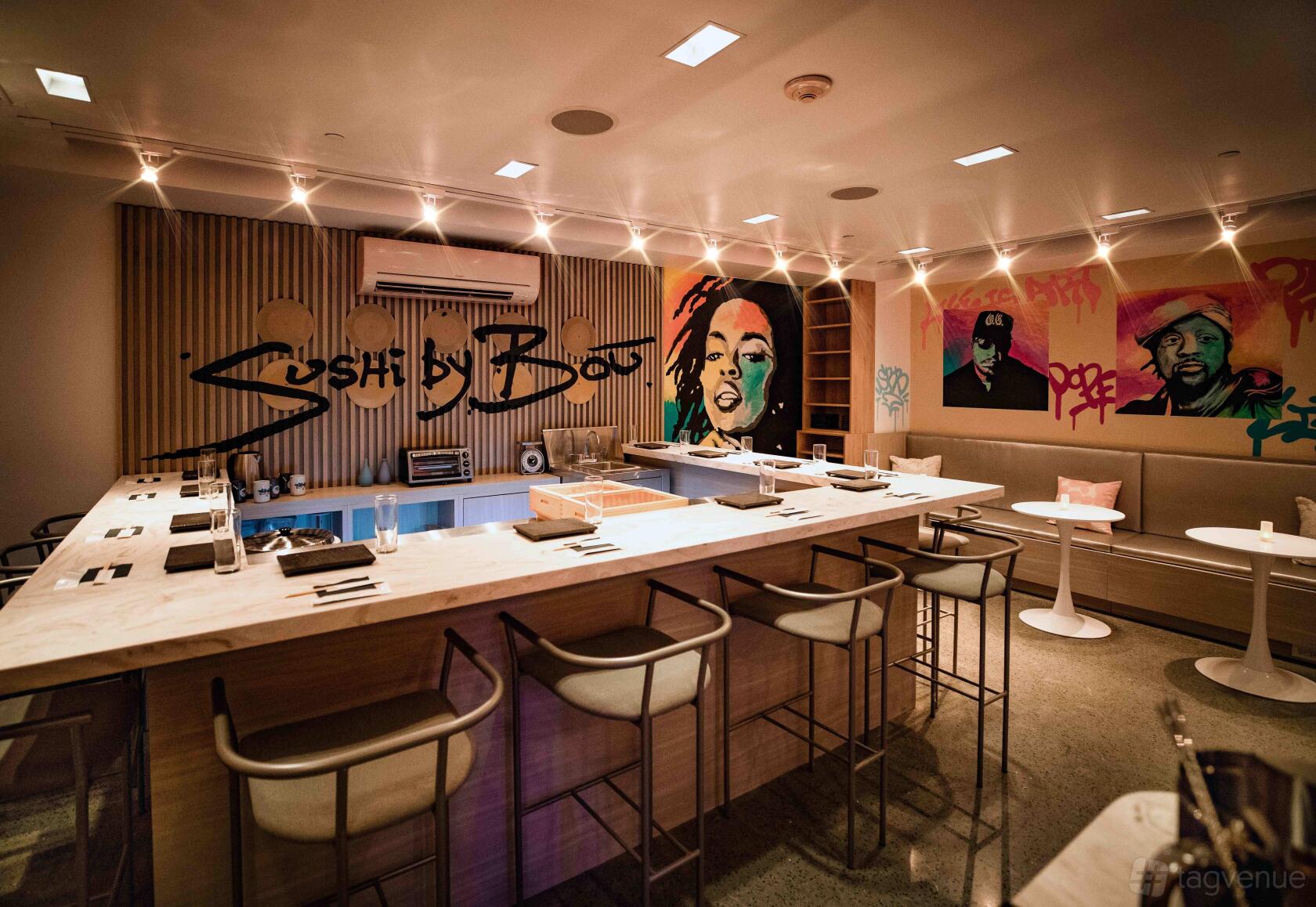 A restaurant with a sushi bar surrounded by high chairs, wall murals, and ambient lighting at Sushi by Bou Hoboken.