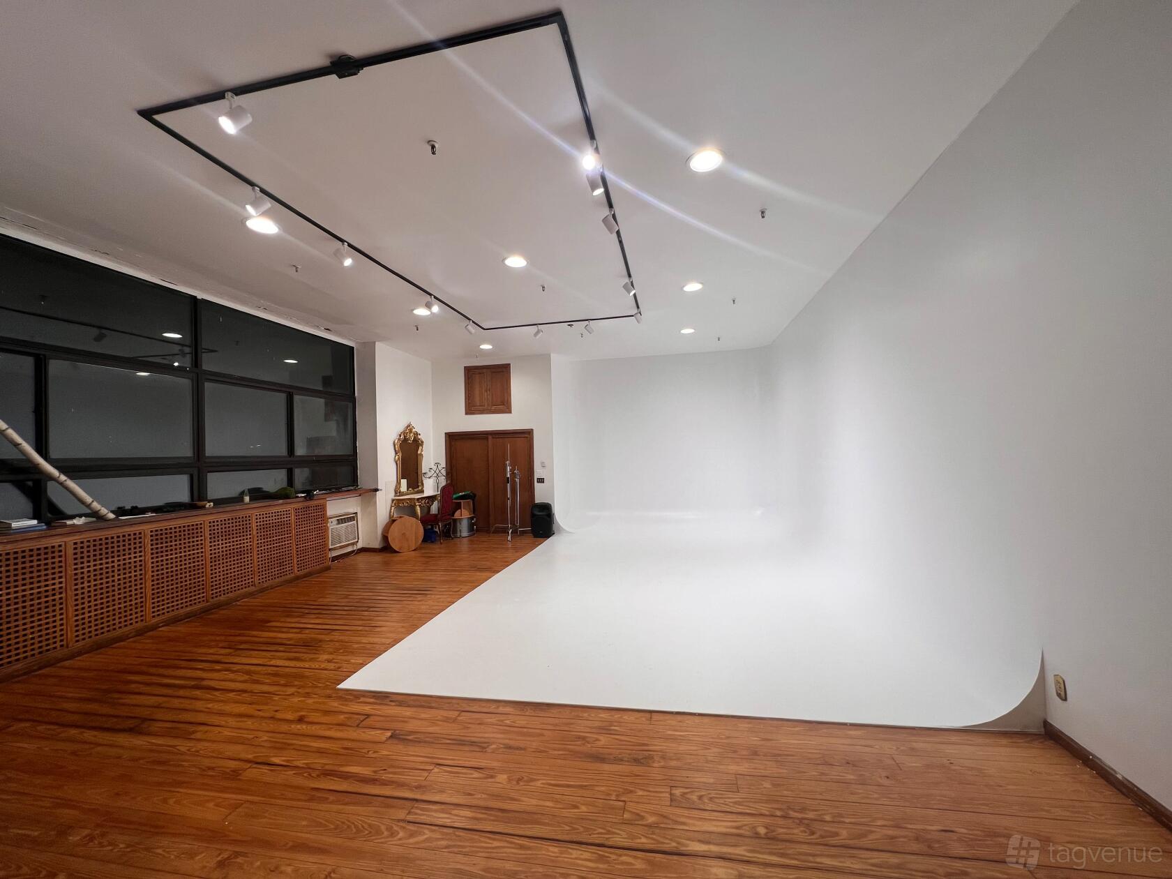 A photo studio with a white cyclorama wall, wood floors, and overhead lighting at IConnect Studios.