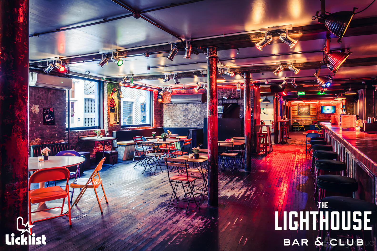 A nightclub with exposed brick walls, colorful neon lighting, and scattered tables with metal chairs at Lighthouse Bar & Nightclub.