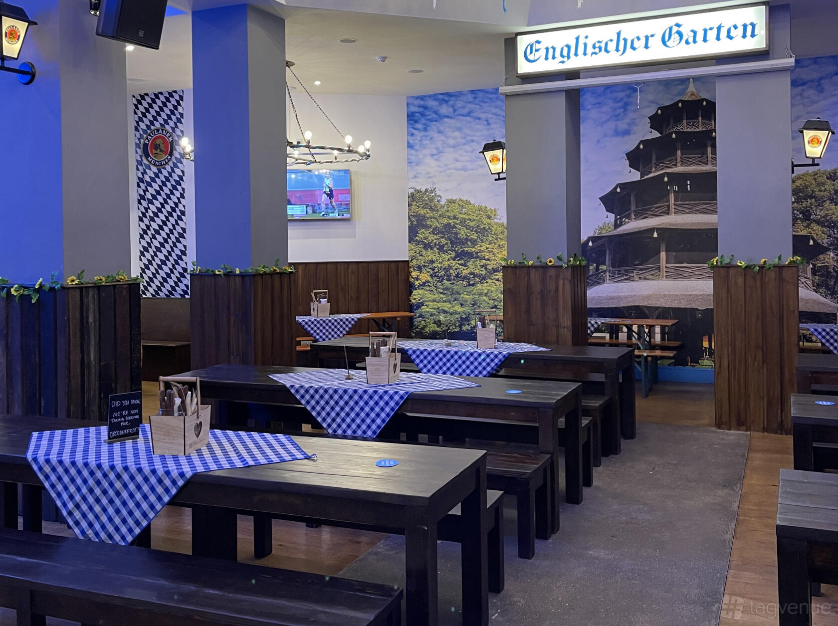 An event space in a restaurant with long wooden tables, blue checkered tablecloths, and Bavarian decor at Munich Cricket Club Victoria.