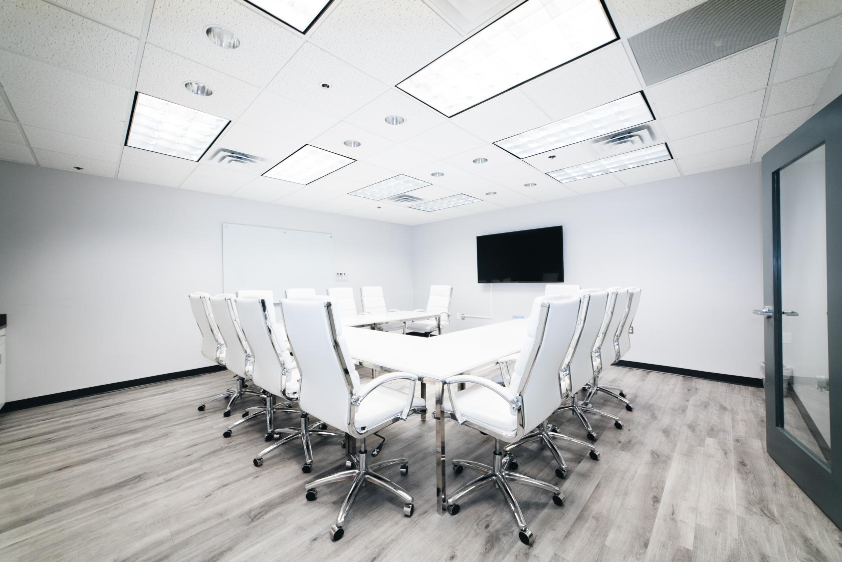 A meeting room with white rolling chairs around a U-shaped table, wall-mounted screen, and whiteboard at Perfect Office Solutions - Laurel II.