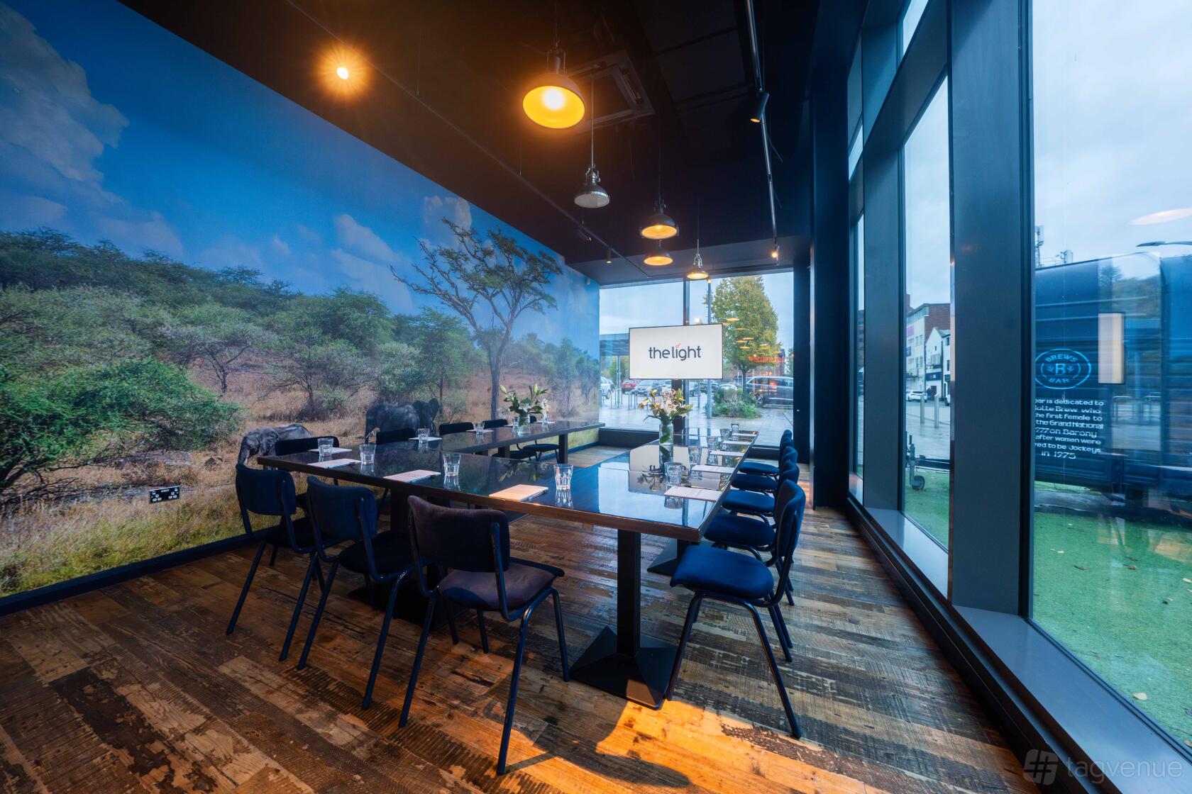 An event space with floor-to-ceiling windows, mural wall, and a long meeting table at The Light Stockport.